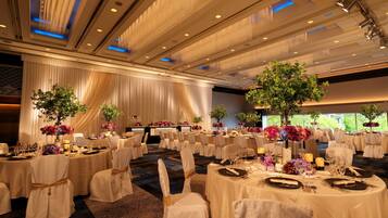 A banquet hall with round tables, white tablecloths, and chairs with gold sashes.