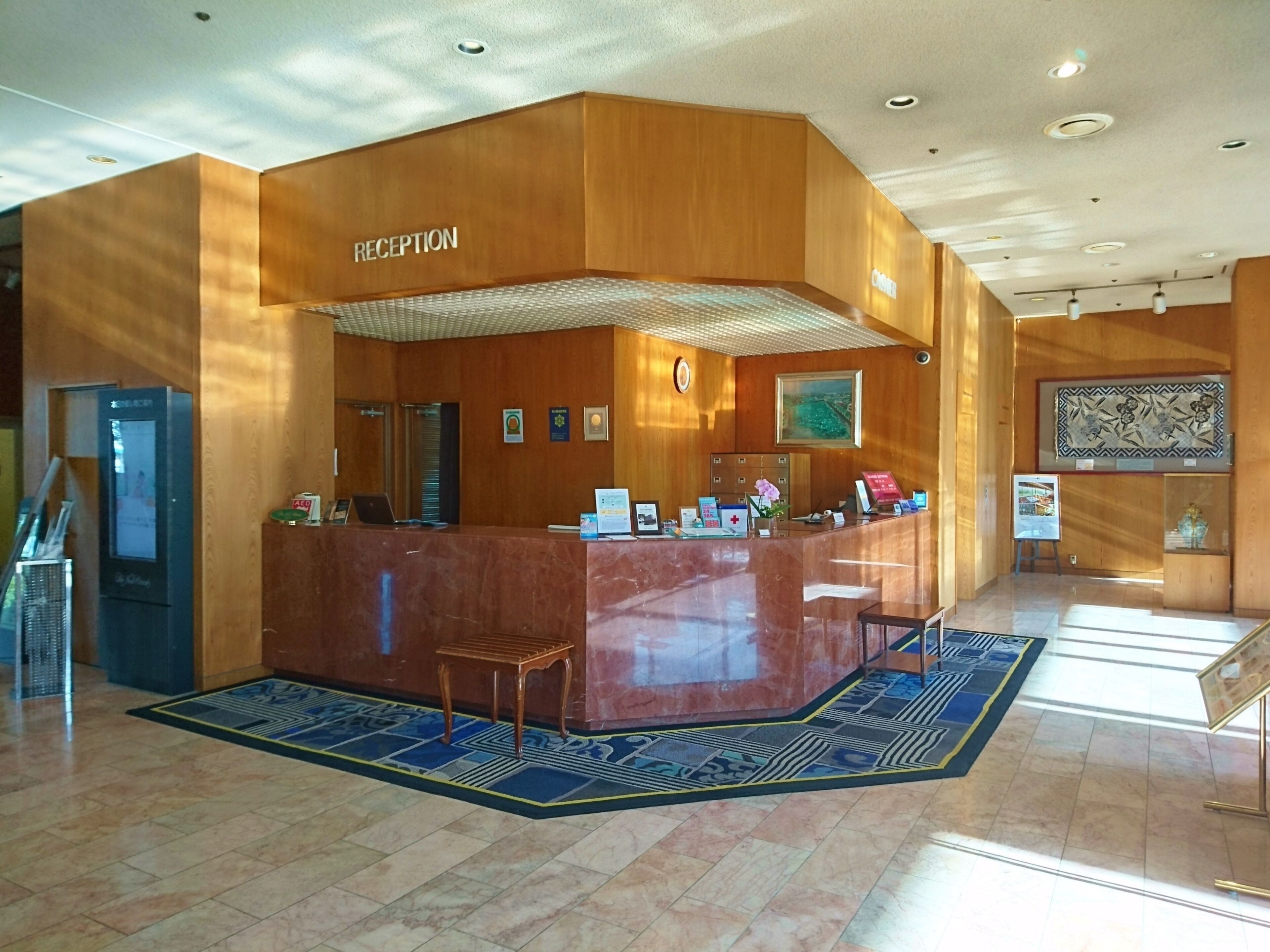 Un área de recepción con un mostrador de madera, un quiosco informativo digital y una alfombra estampada.