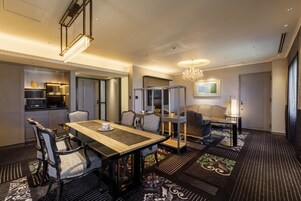 A hotel room with a dining area, a sofa set, a chandelier, and a patterned carpet.
