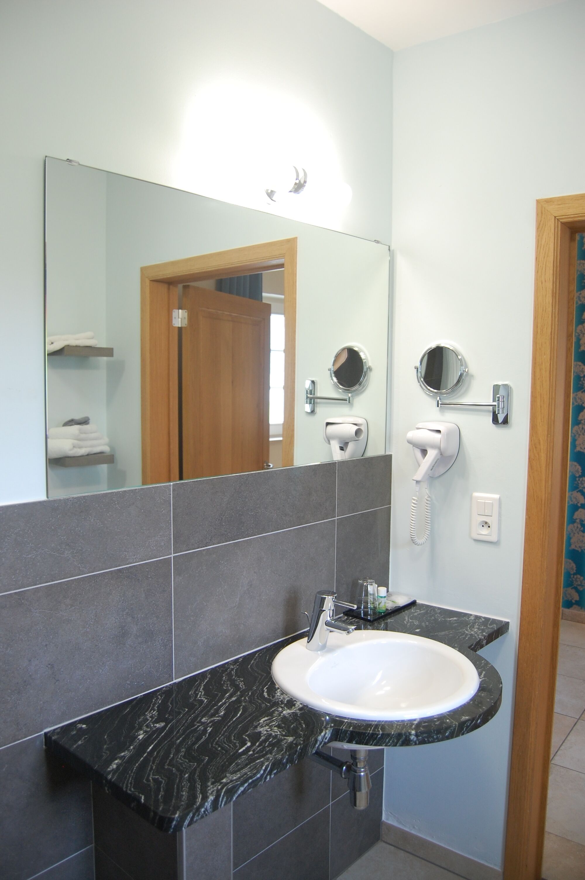 A bathroom with a marble sink, a mirror, a hairdryer, and a towel rack.