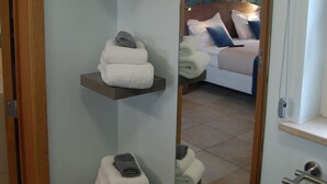 Un bagno con uno specchio che riflette una camera da letto. Si vedono tre portasci con asciugamani piegati.
