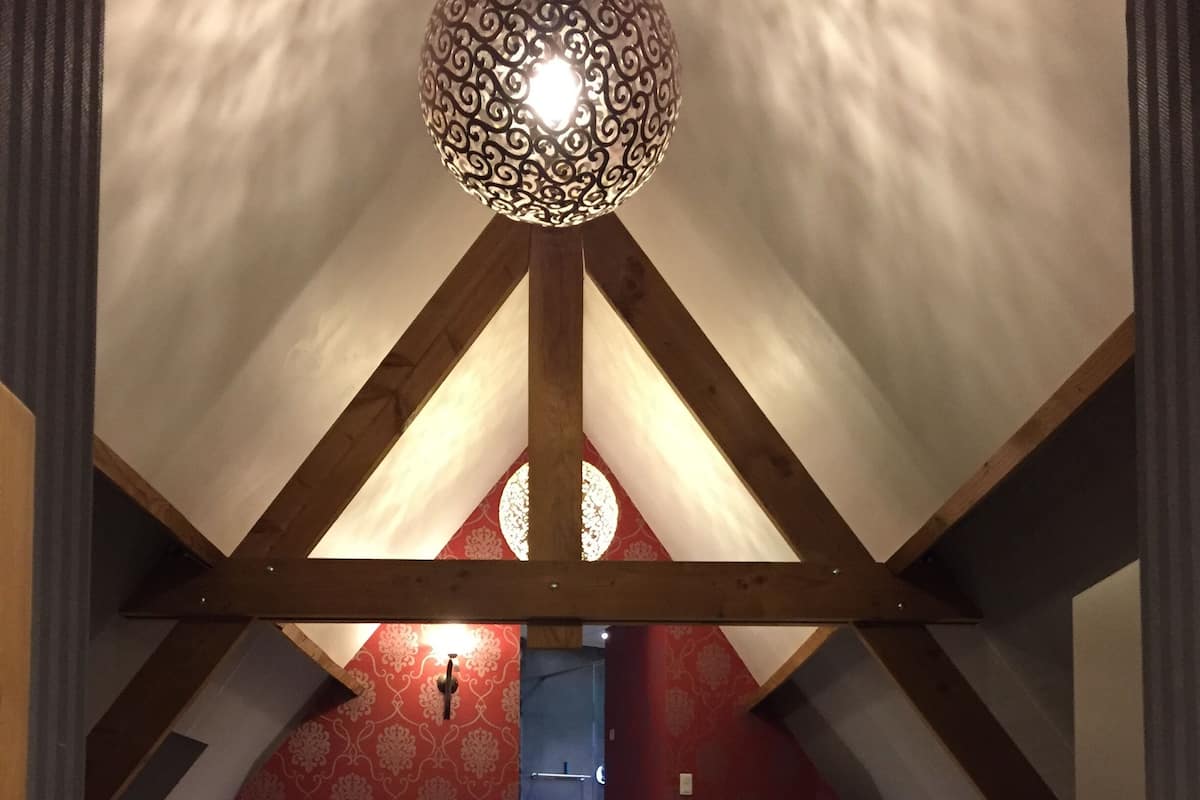 Een slaapkamer met een gewelfd plafond, een groot bed met rode kussens, twee bedlampen en een decoratieve plafondlamp.