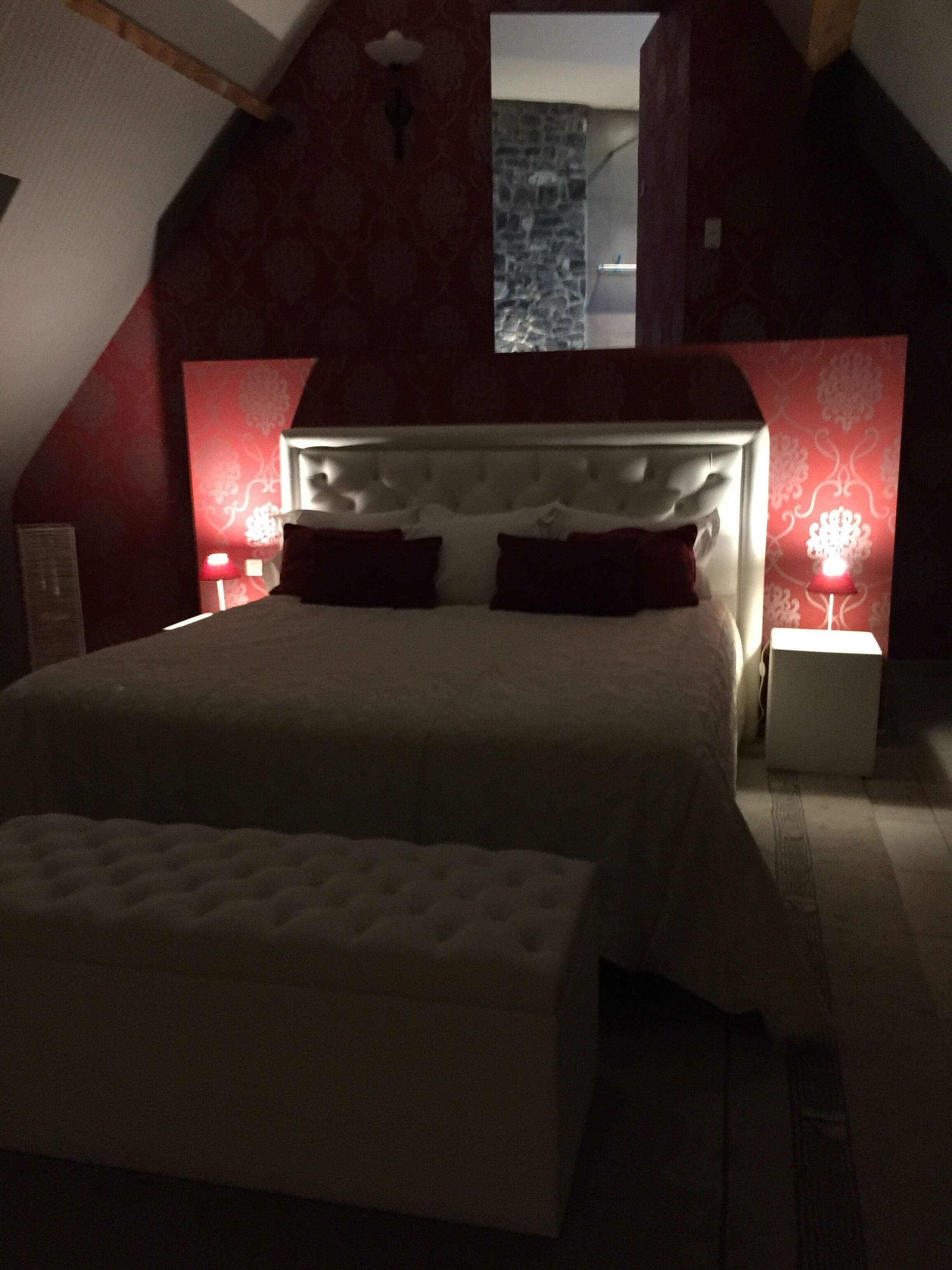 A bedroom with a large bed, red walls, and a sloped ceiling.