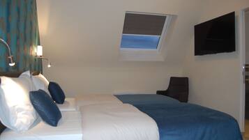 Quarto de hotel com cama, poltrona, televisão, janela e cortina.