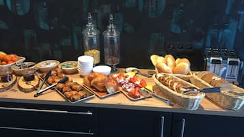 Un bufé con diferentes opciones de comida, entre ellas frutas, pasteles y pan.