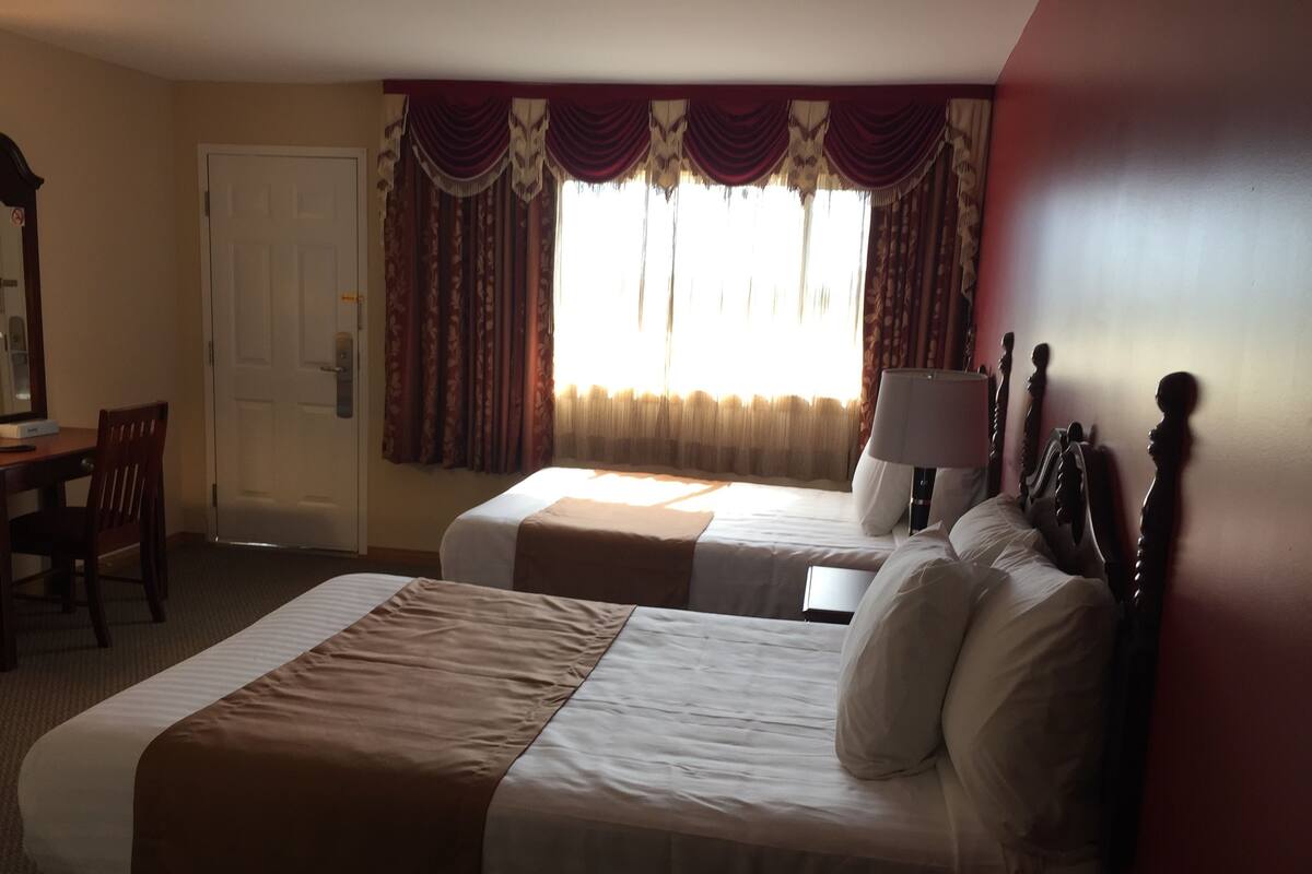 A hotel room with two beds, a desk with a chair, a lamp, and a mirror.