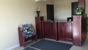 A reception desk with a magazine rack, a potted plant, and a dark mat in a hotel lobby.