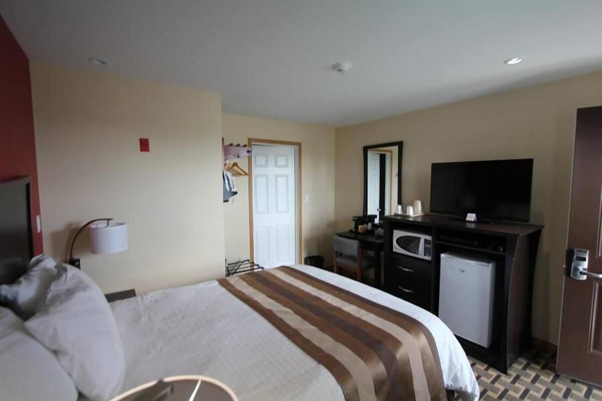A hotel room with a bed, a desk with a computer, a television, and a door.