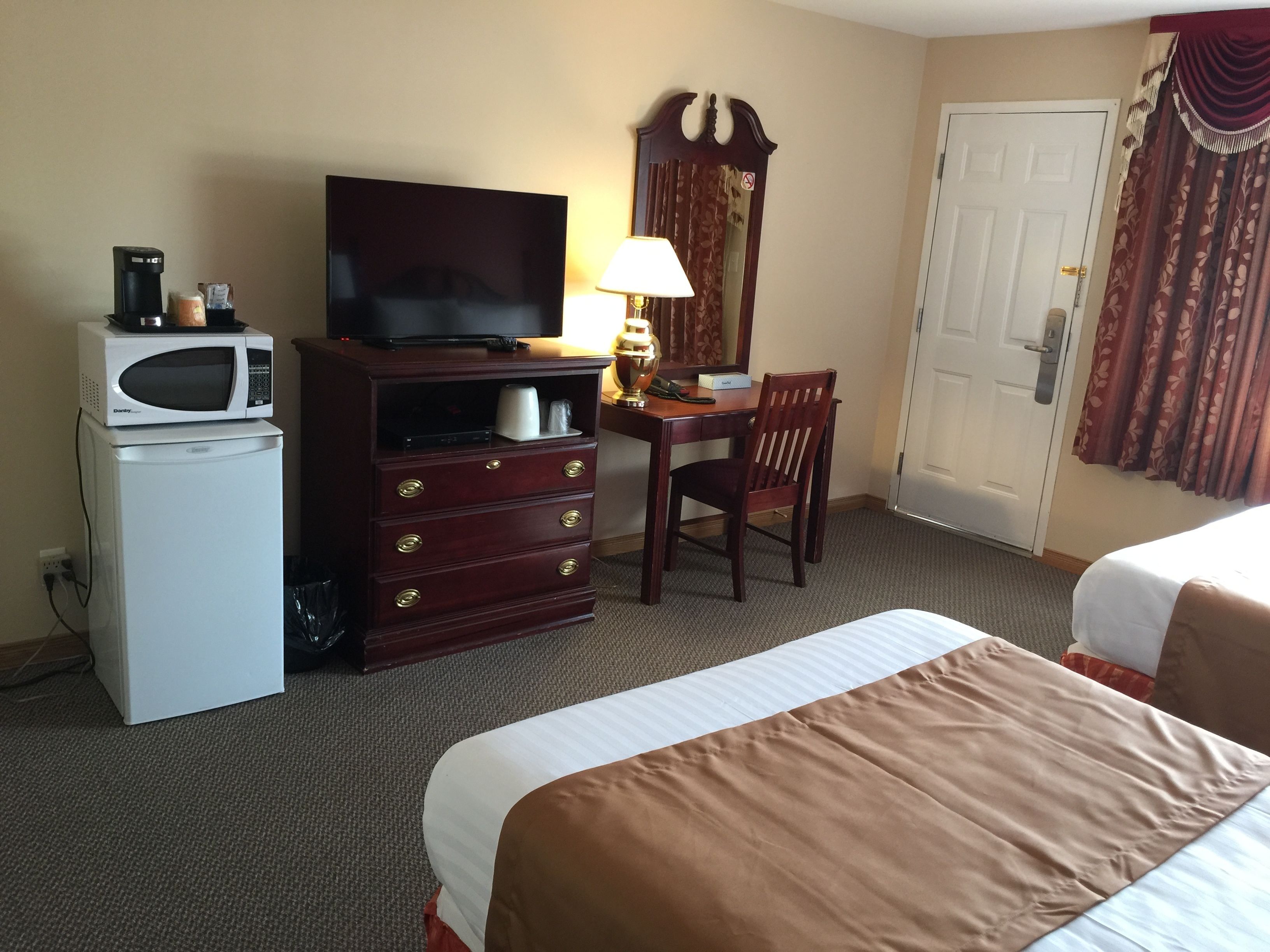 A hotel room with a bed, a desk with a chair, a television, a microwave, and a refrigerator.