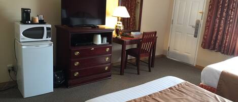 A hotel room with a bed, a desk with a chair, a television, a microwave, and a refrigerator.