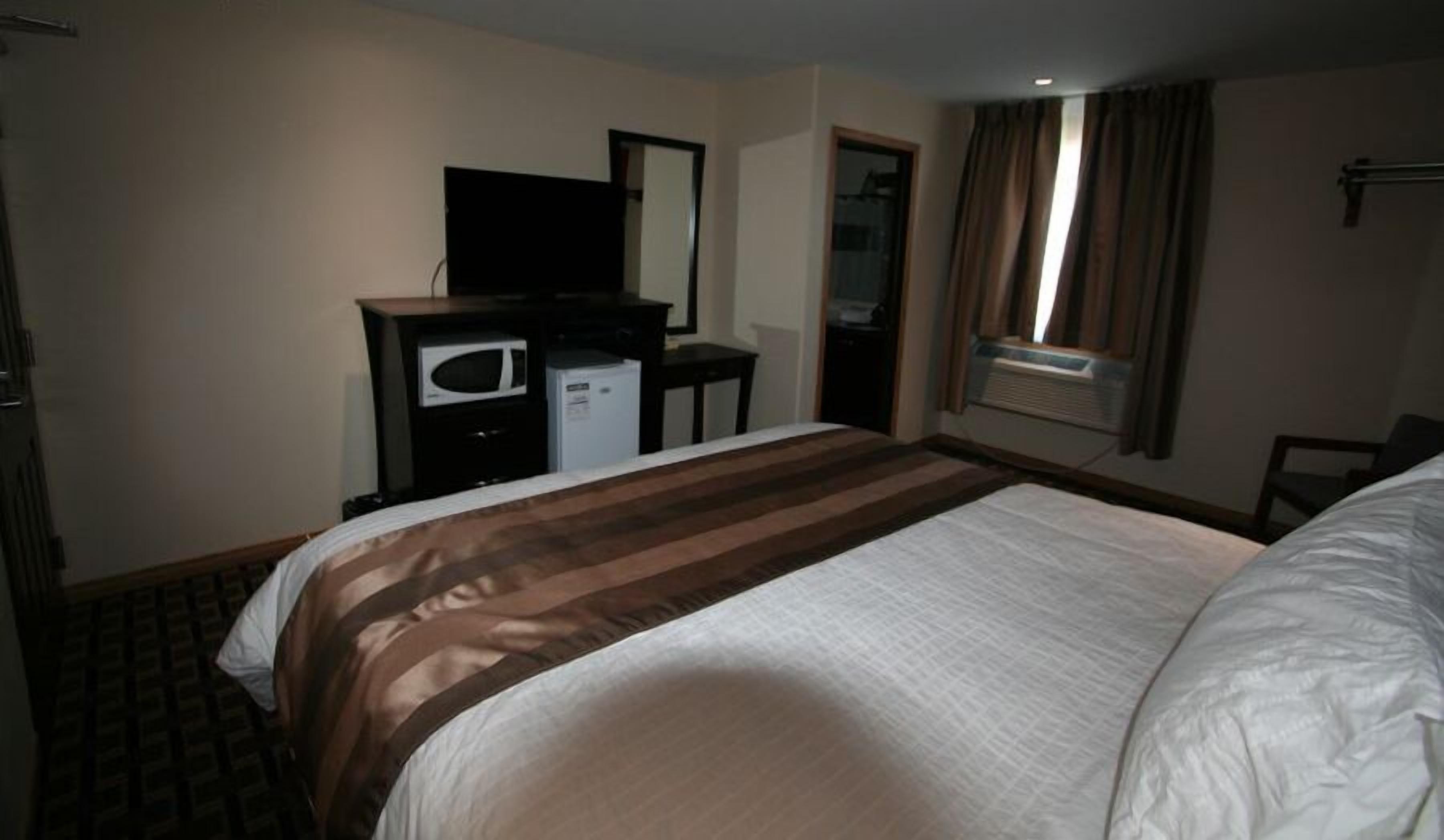 A hotel room with a large bed, a desk with a television, a microwave, and a small refrigerator.