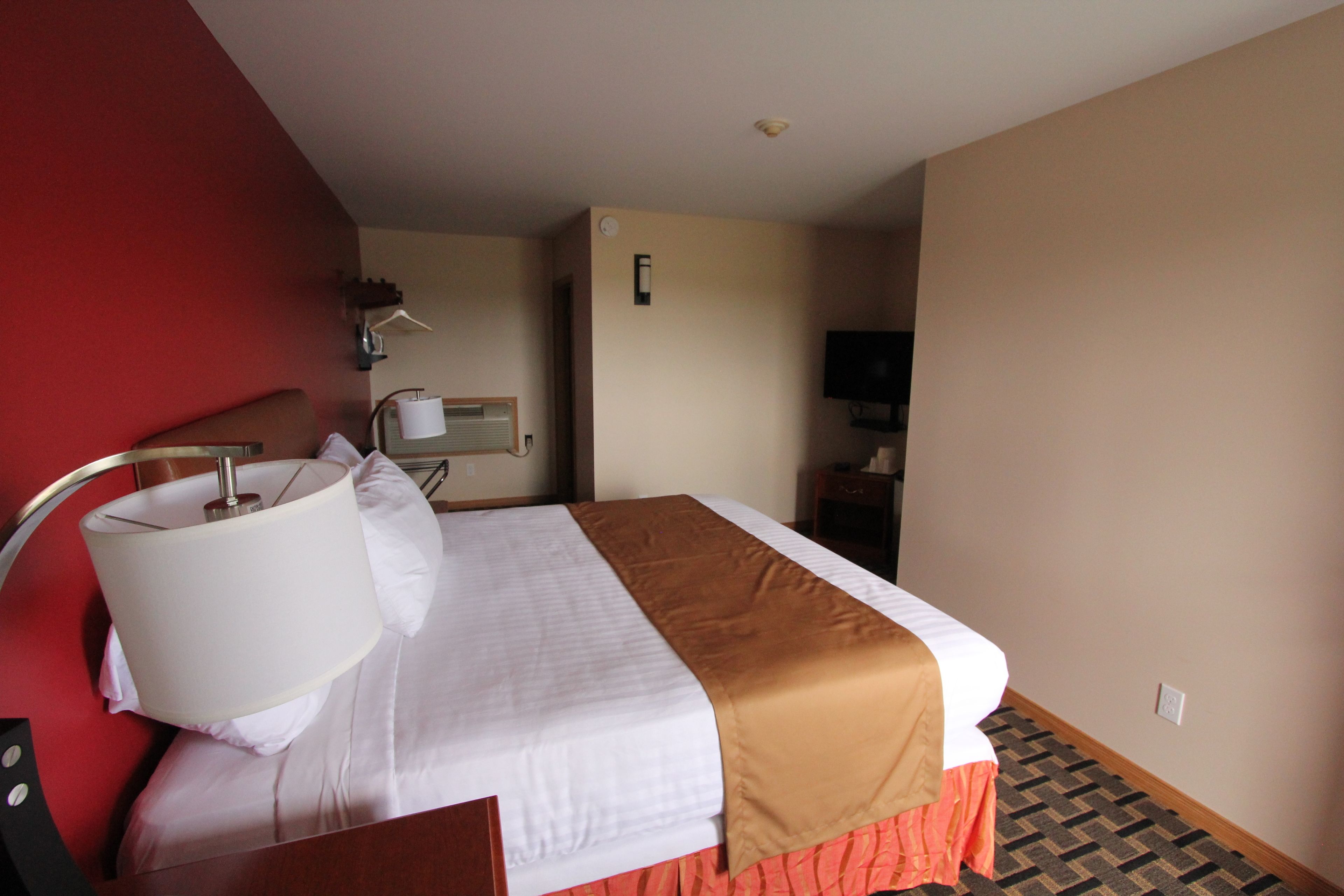 Una habitación de hotel con una cama, una lámpara, un televisor y una pared roja.