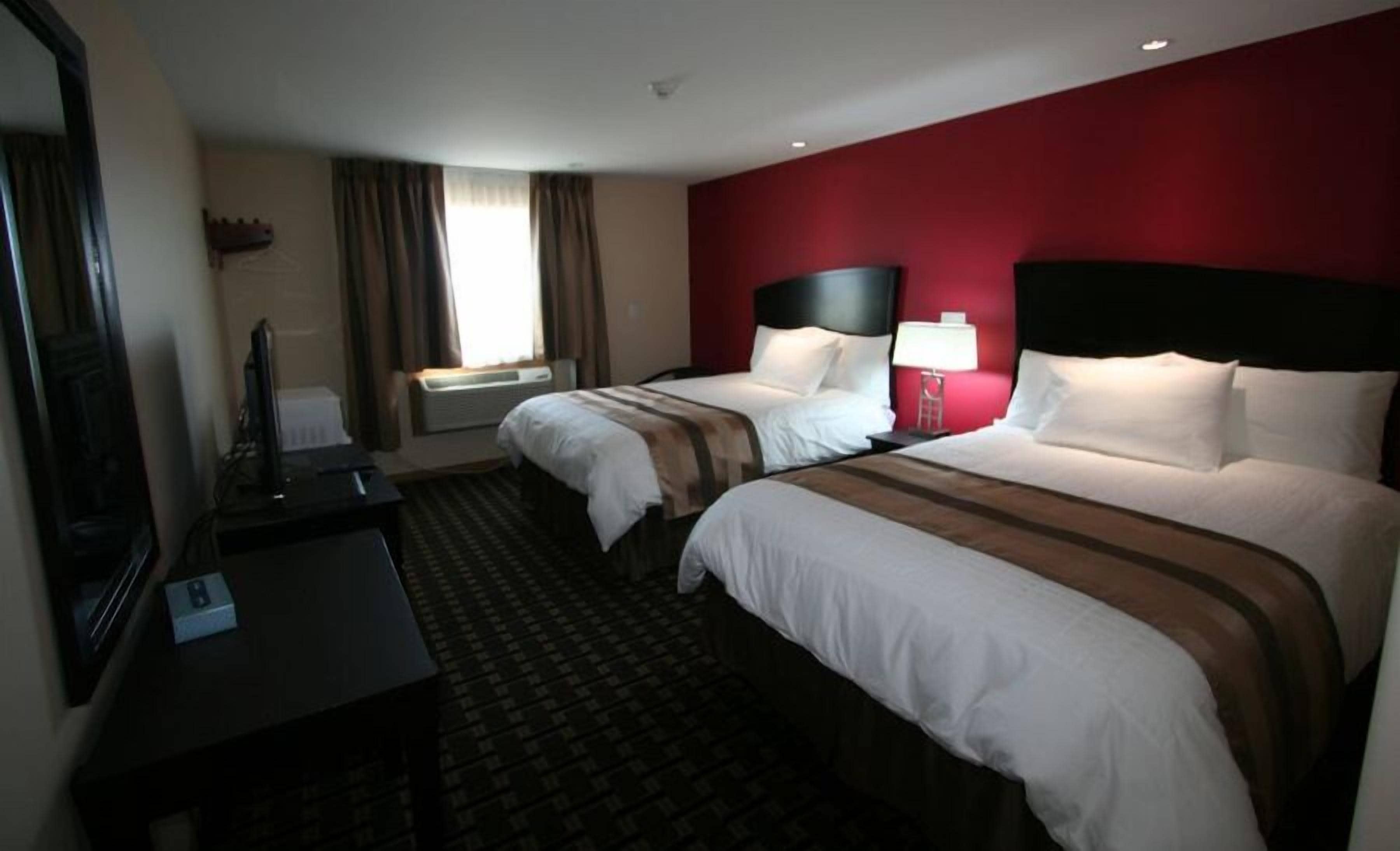 Habitación de hotel con dos camas, un escritorio, un televisor y una ventana con cortinas.
