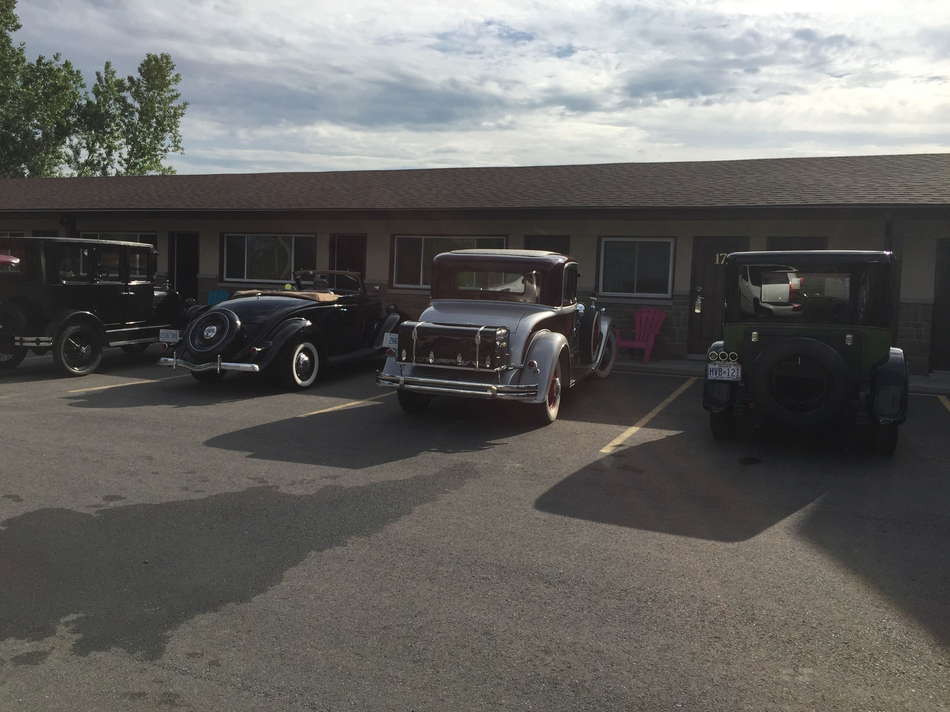 A parking lot with several vintage cars parked in front of a building with a brick facade and large windows.