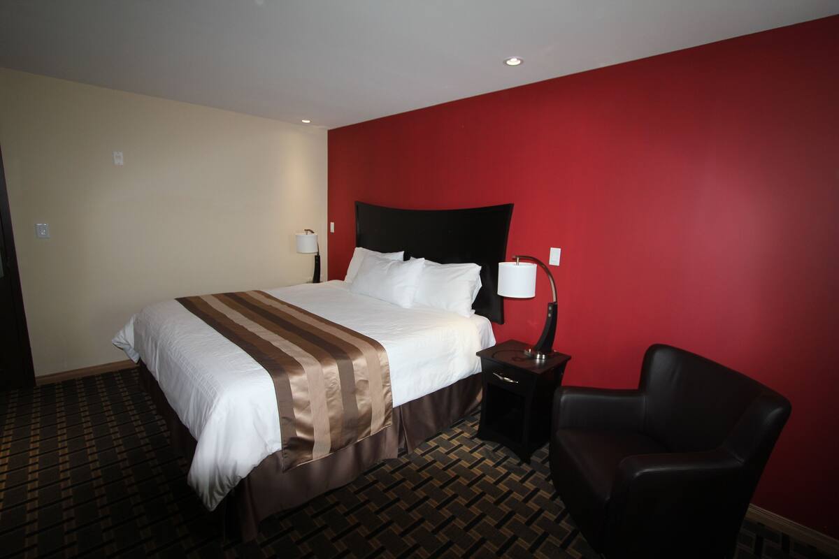 A hotel room with a large bed, a nightstand, a chair, and a red accent wall.