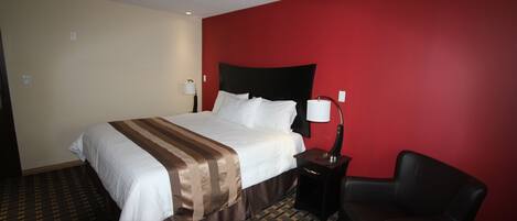 Habitación de hotel con una cama grande, una mesita de noche, una silla y una pared de acento roja.