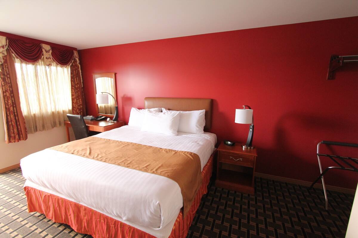 A hotel room with a large bed, a desk, a chair, a lamp, and a mirror.