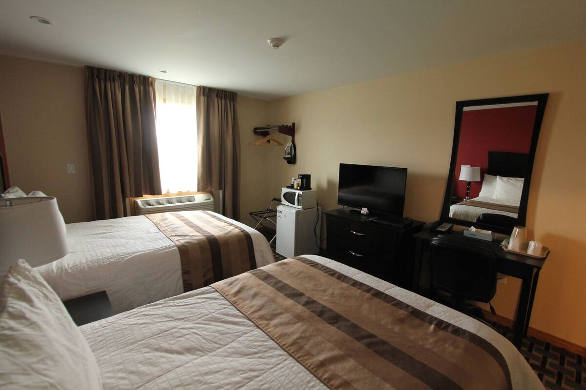A hotel room with two beds, a desk, a television, and a mirror.
