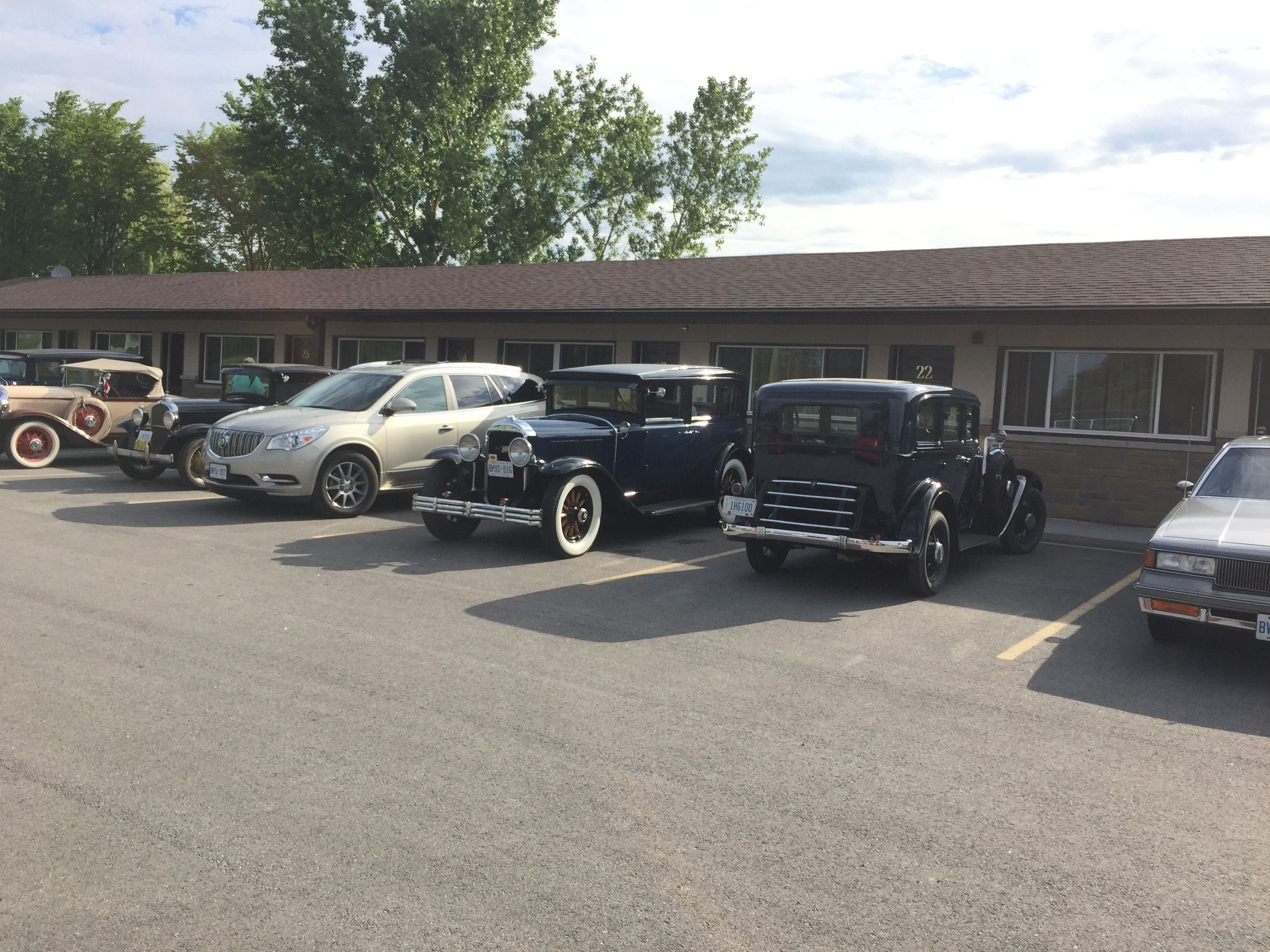 Een parkeerplaats met verschillende oldtimers voor een gebouw met een bakstenen gevel en grote ramen.