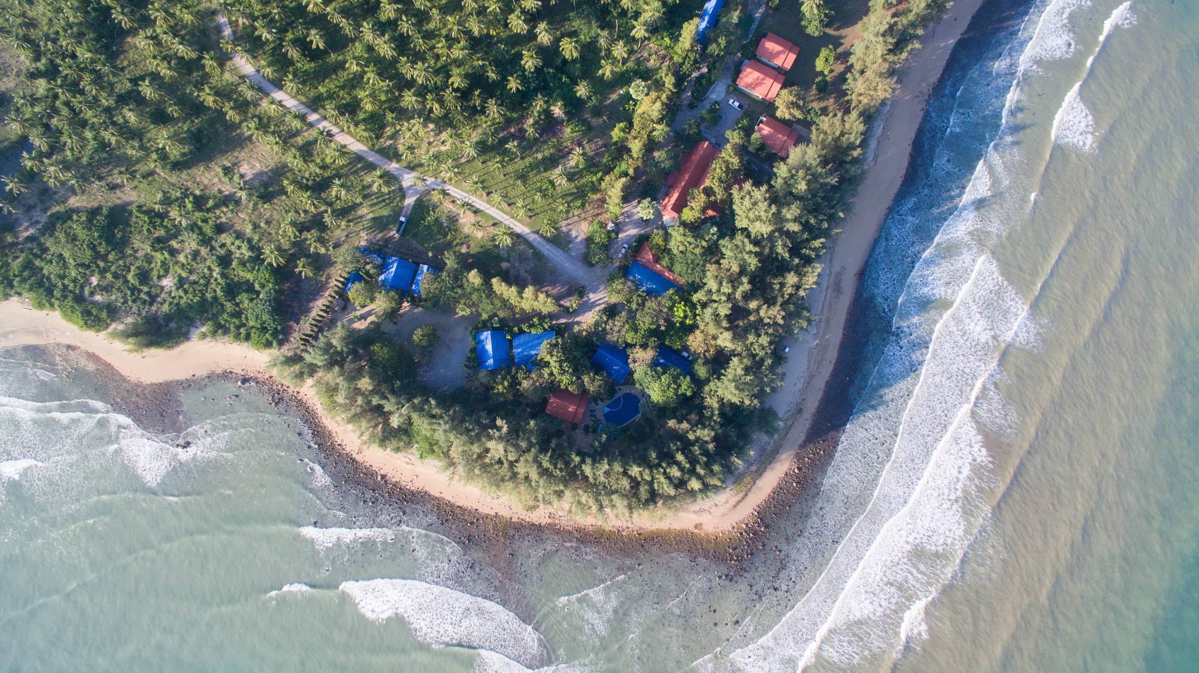 Vista aérea de una zona costera con playa, carretera y varios edificios con techos rojos.