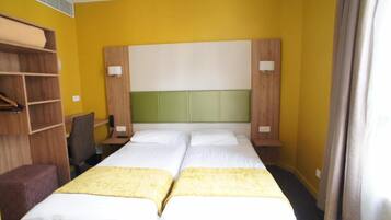 Habitación de hotel con dos camas, un escritorio, una silla y un armario.