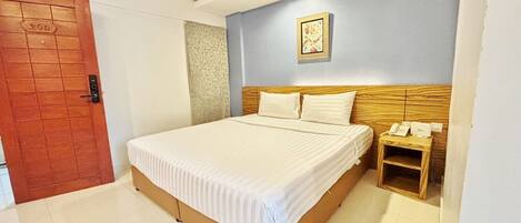 Habitación de hotel con una cama, cabecera de madera, mesita de noche con un teléfono y una puerta con un número.