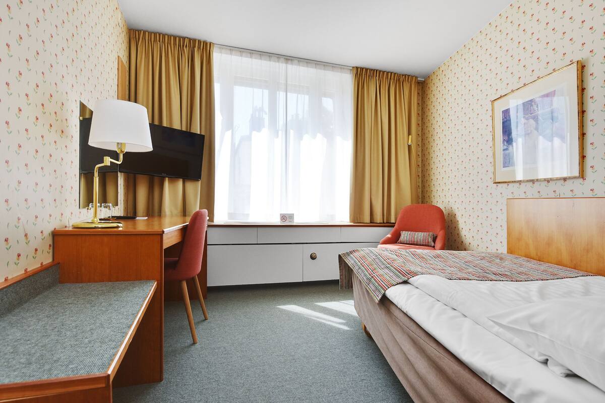 Una habitación de hotel con cama, escritorio, silla y televisor.