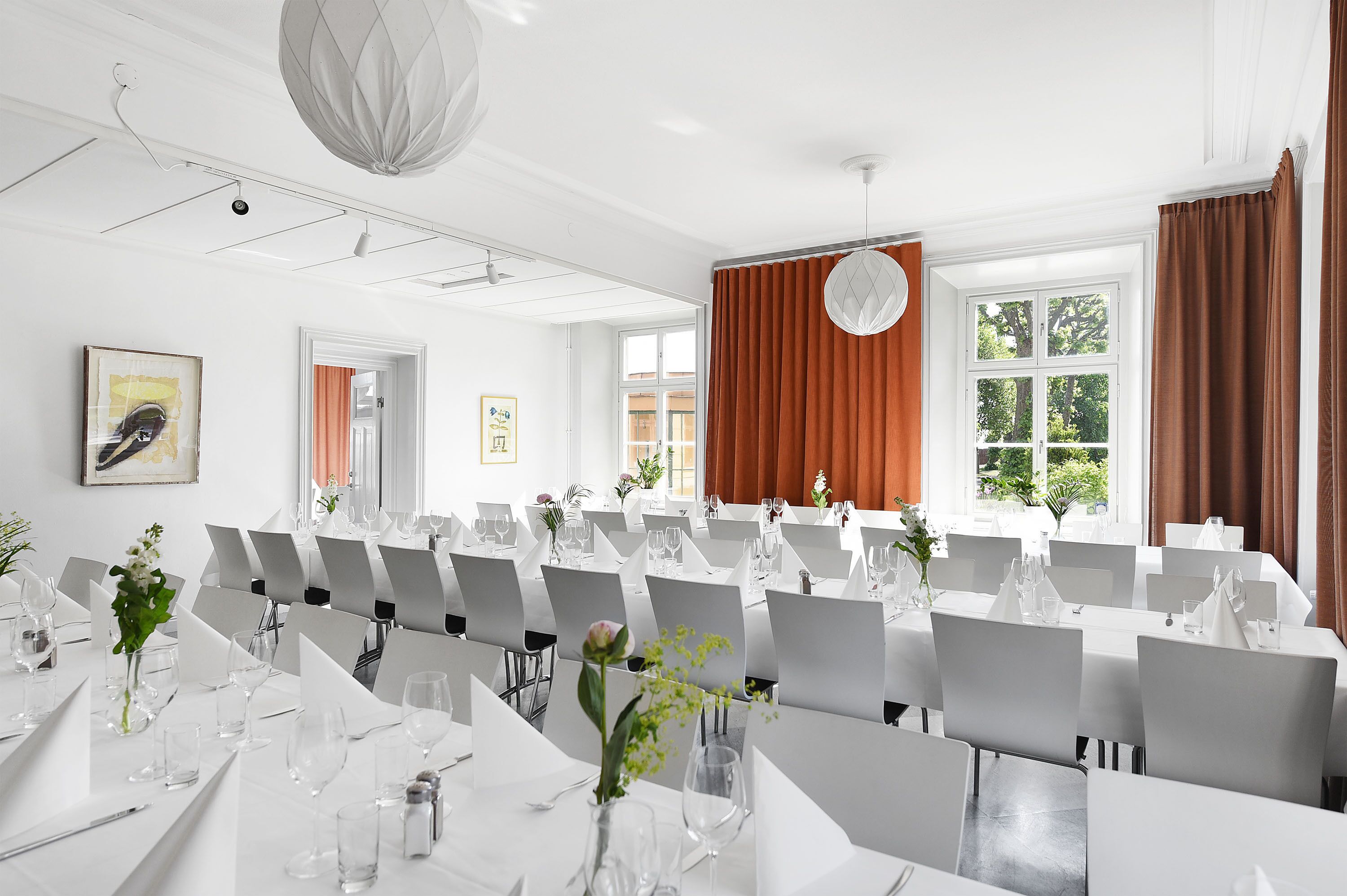 A conference room with white tables, chairs, and a large window with curtains.