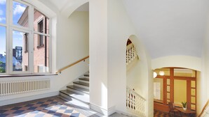 Un pasillo amplio con piso a cuadros, una escalera y vistas de los edificios exteriores.