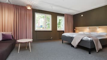 A modern hotel room with a bed, a sofa, a small table, and large windows.