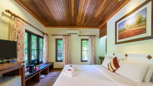 A hotel room with a wooden ceiling, a bed with white linens, a painting on the wall, and a desk with a television. - Baan Grood Arcadia Resort & Spa (Bang Saphan)