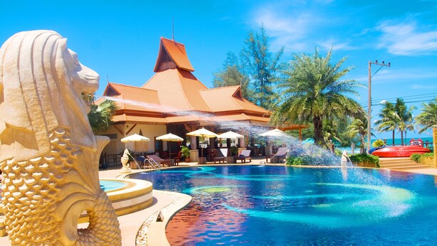 A swimming pool with a water feature, a large stone lion statue, and a building with a red roof. - Baan Grood Arcadia Resort & Spa (Bang Saphan)