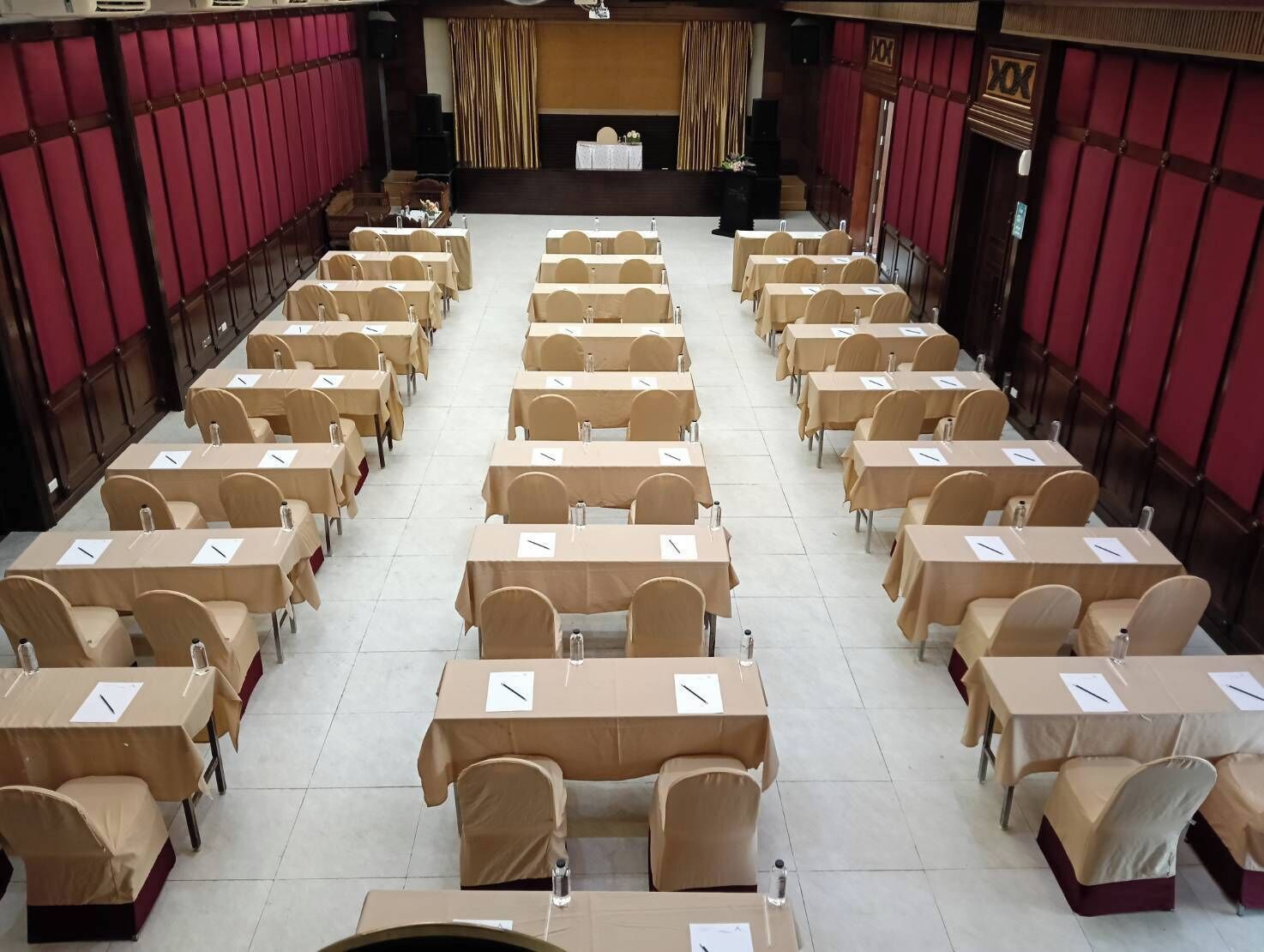 A conference room with rows of tables and chairs, a stage at the front, and red curtains on the walls.