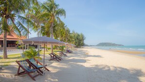 A beach with lounge chairs and umbrellas, palm trees, and a clear view of the ocean. - Baan Grood Arcadia Resort & Spa (Bang Saphan)