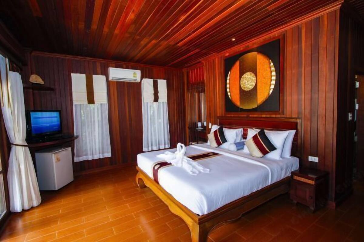 Une chambre d’hôtel avec un plafond en bois, un lit avec du linge de maison blanc, une télévision et un appareil de climatisation.