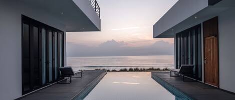 Una piscina infinita moderna con vistas despejadas al océano y montañas al fondo.