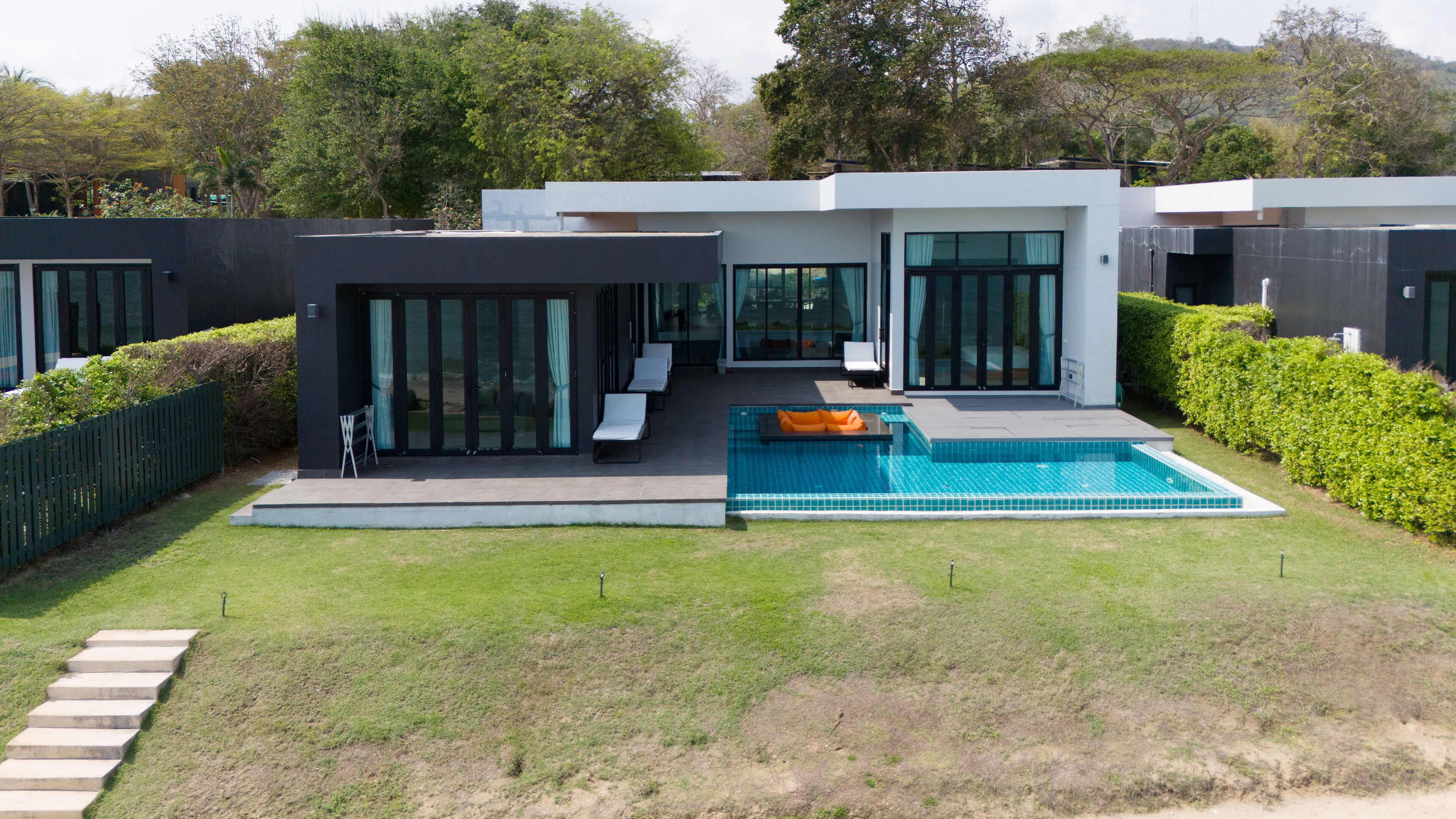 Una casa moderna con piscina, puertas de cristal y césped bien cuidado.