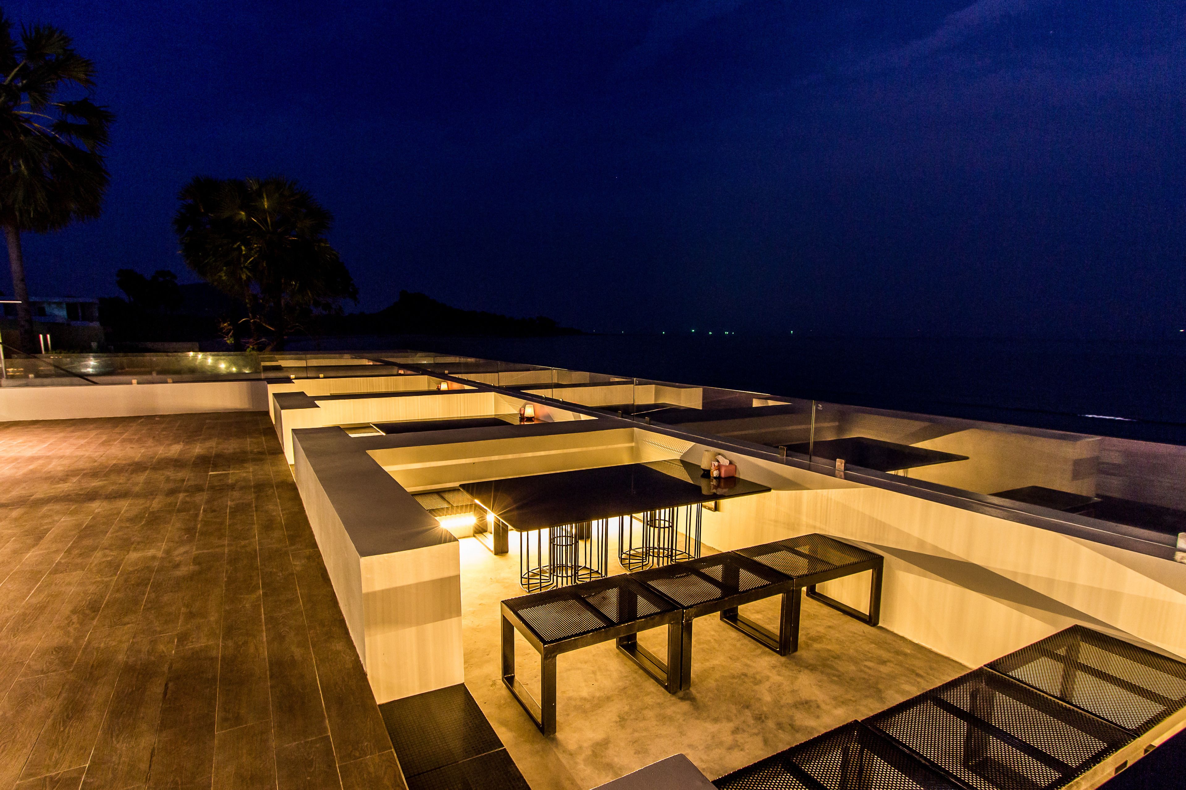 An outdoor terrace with a pool table, seating area, and a view of the ocean at night.