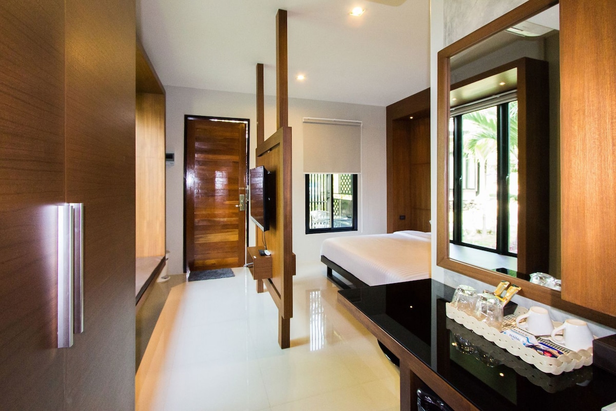A modern hotel room with a wooden wardrobe, a bed with white bedding, a large mirror, and a breakfast tray on the counter.
