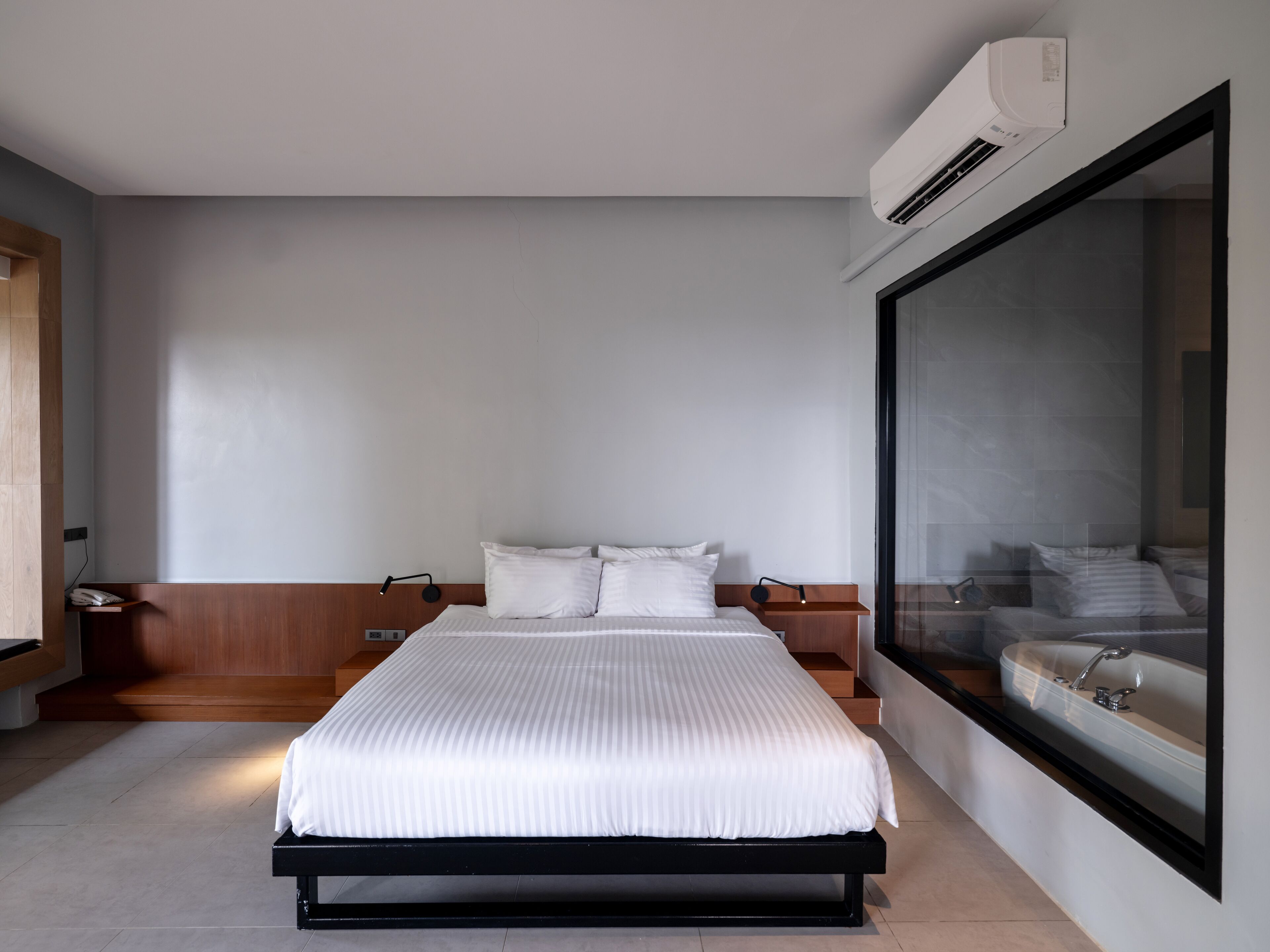 A modern hotel room with a large bed, a nightstand, a bedside table, a large window, and a built-in sink.