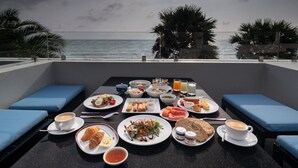 A dining table with various dishes and drinks, overlooking the ocean. - Sunshine Paradise Resort (Thap Sakae)