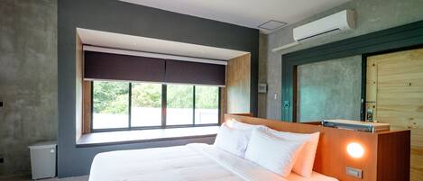 Una habitación de hotel moderna con una cama grande, una ventana con vistas, un equipo de aire acondicionado y una puerta de madera.