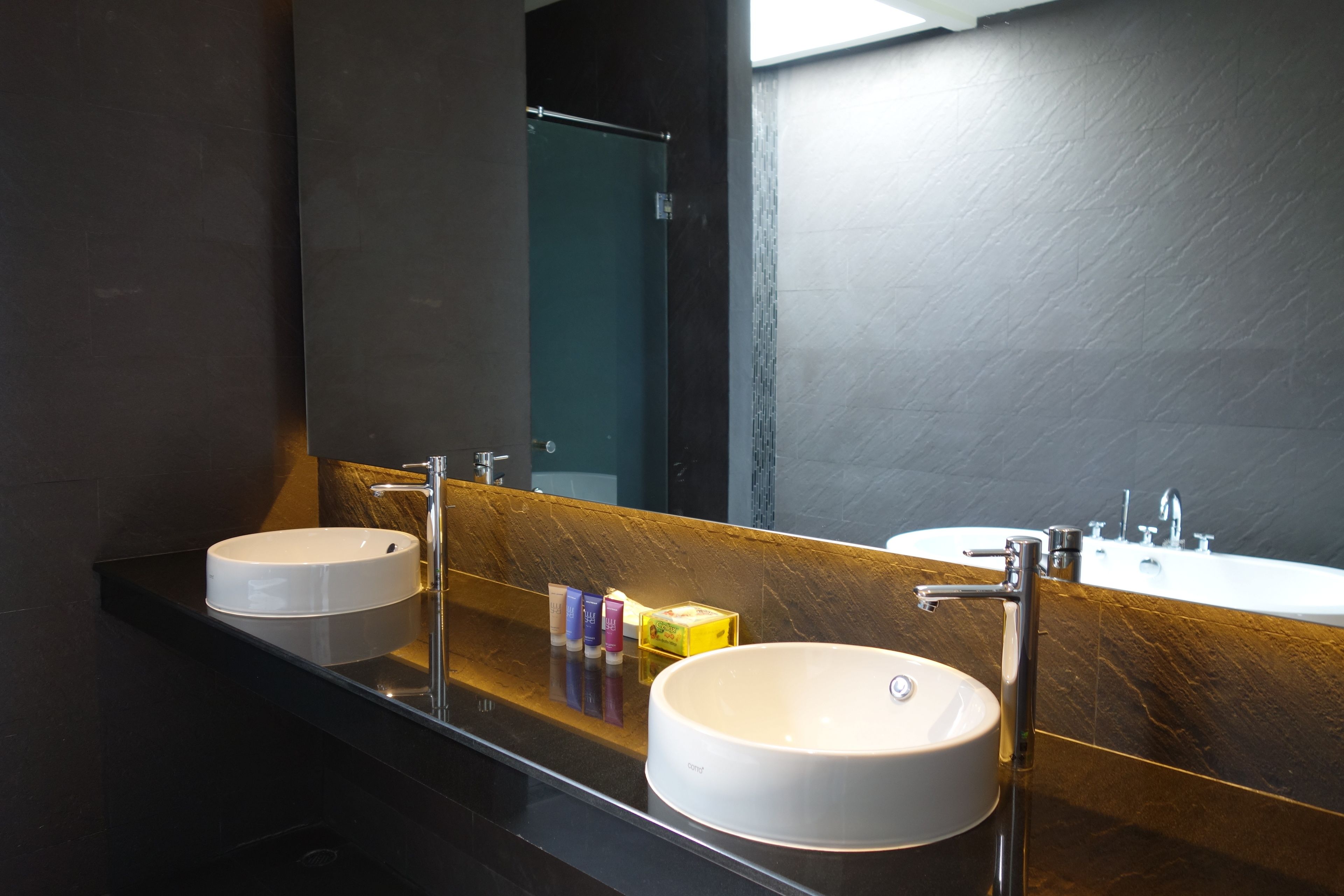 Un baño moderno con dos lavamanos, un espejo grande y artículos de aseo en la encimera.