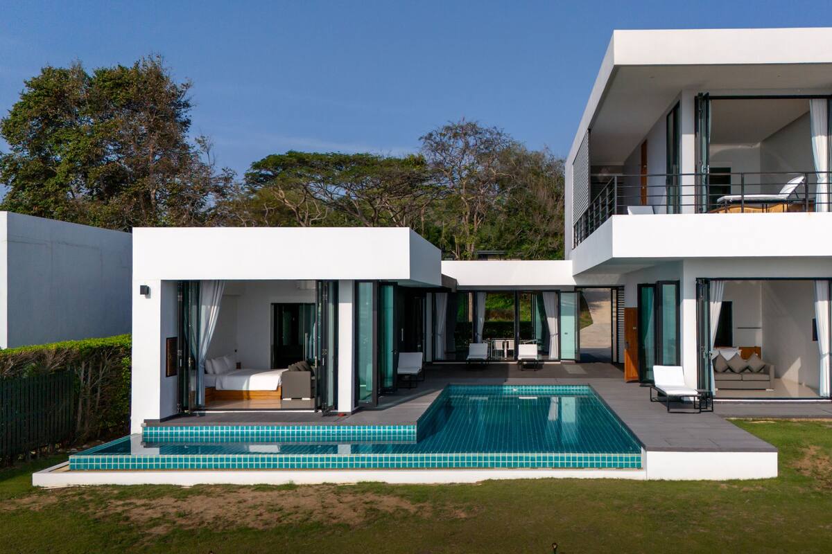 A modern two-story house with a swimming pool, large glass doors, and a balcony.