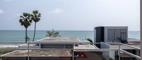 A modern outdoor seating area with a red sofa, overlooking a beach and ocean.