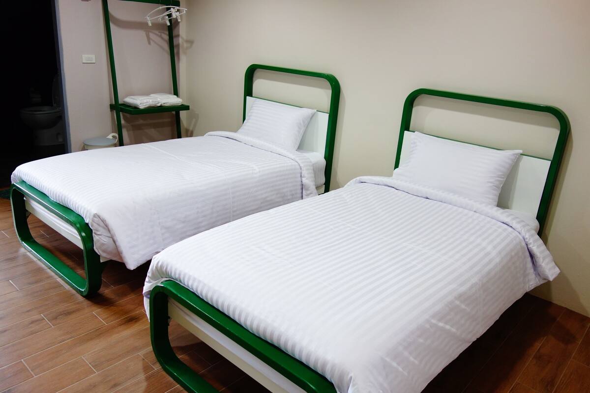 Two single beds with green frames and white bedding in a room with wooden flooring.