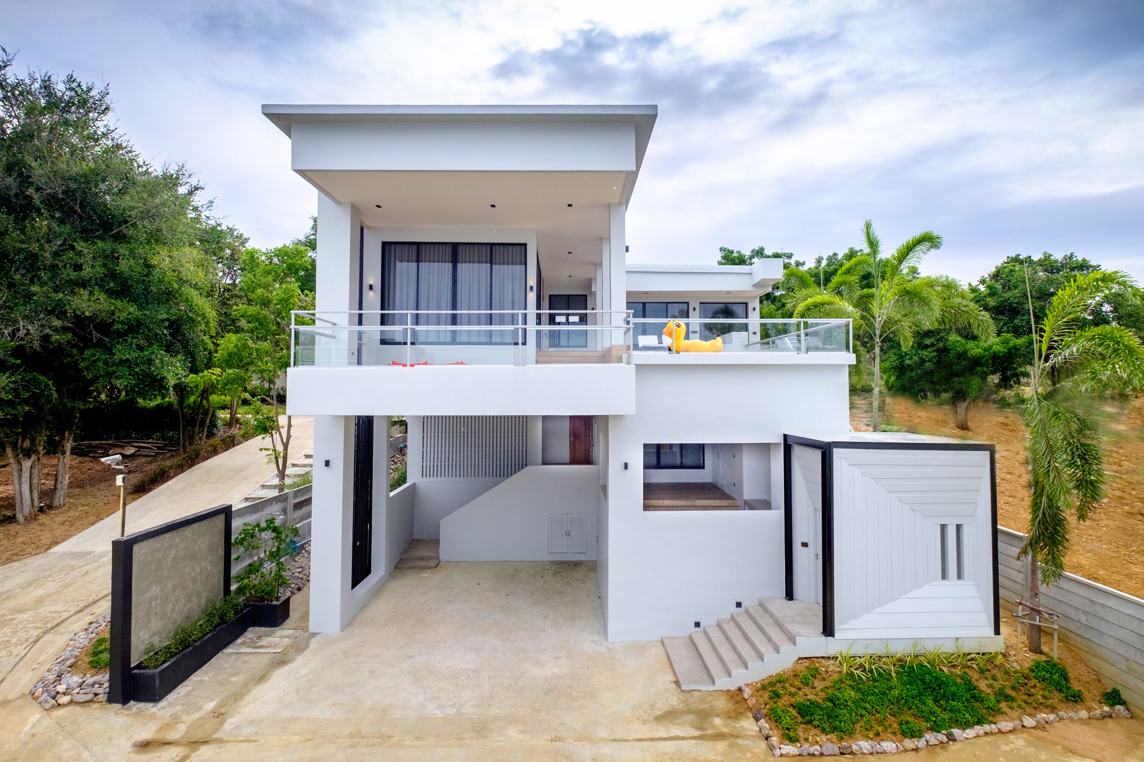 A modern two-story house with a balcony, a staircase, and a garden area.