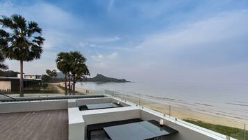 A rooftop terrace with a view of the beach, palm trees, and a distant mountain.