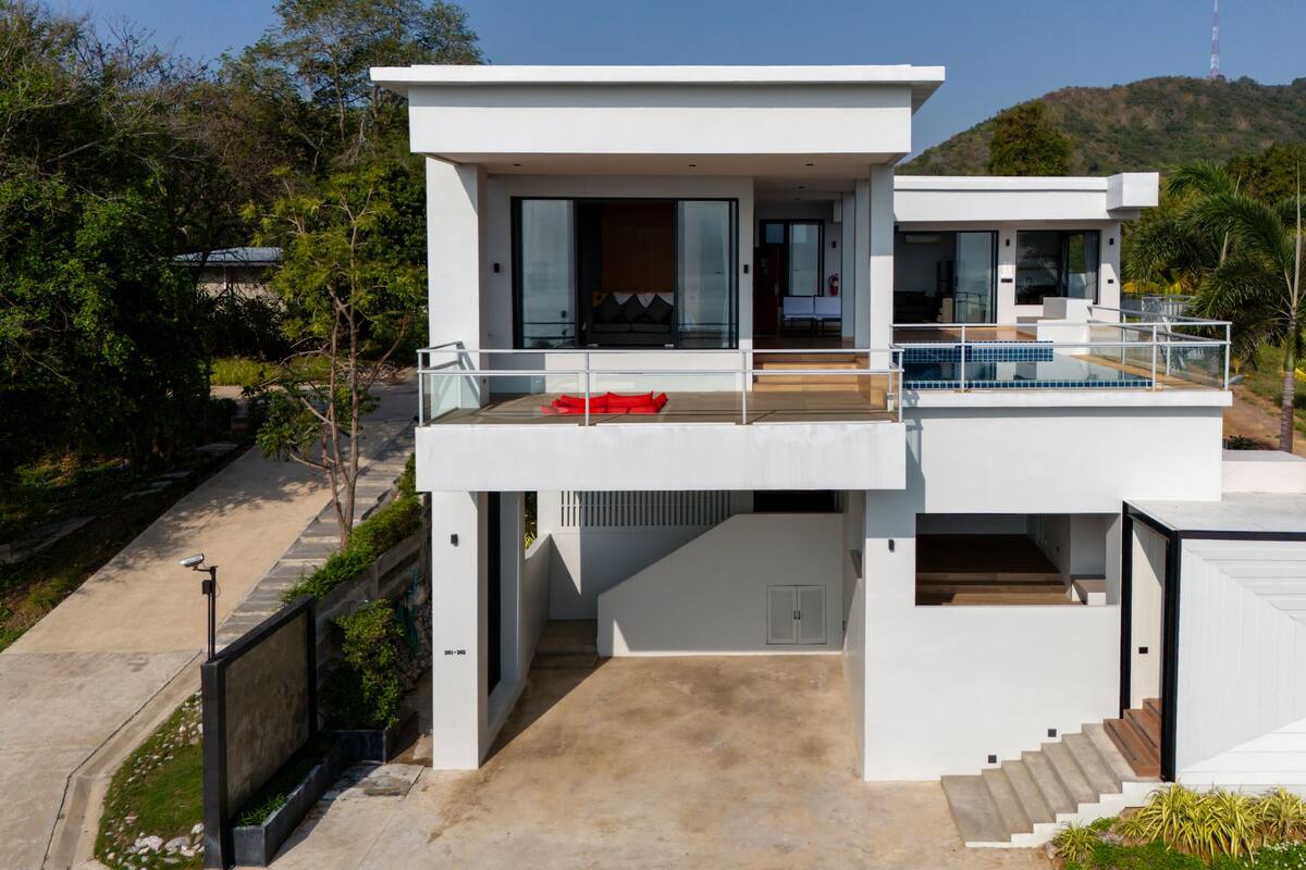 A modern two-story house with a balcony, a pool, and a view of a hill.
