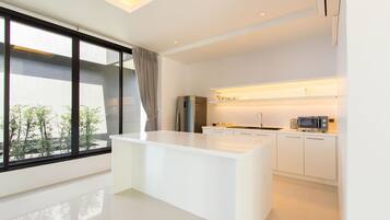 A modern kitchen with a central island, white cabinetry, and a large window offering a view of greenery.